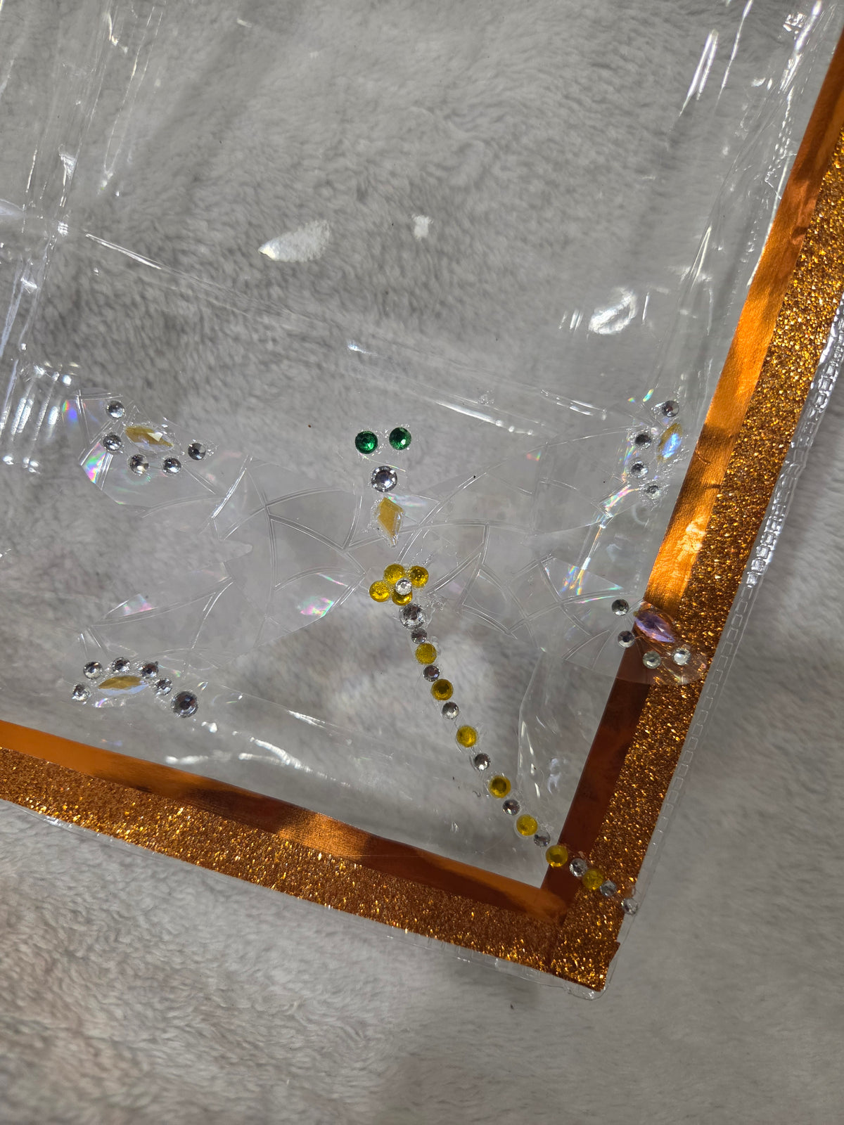 Close-up of hand-rhinestoned dragonfly on clear PVC bag with gold glitter trim
