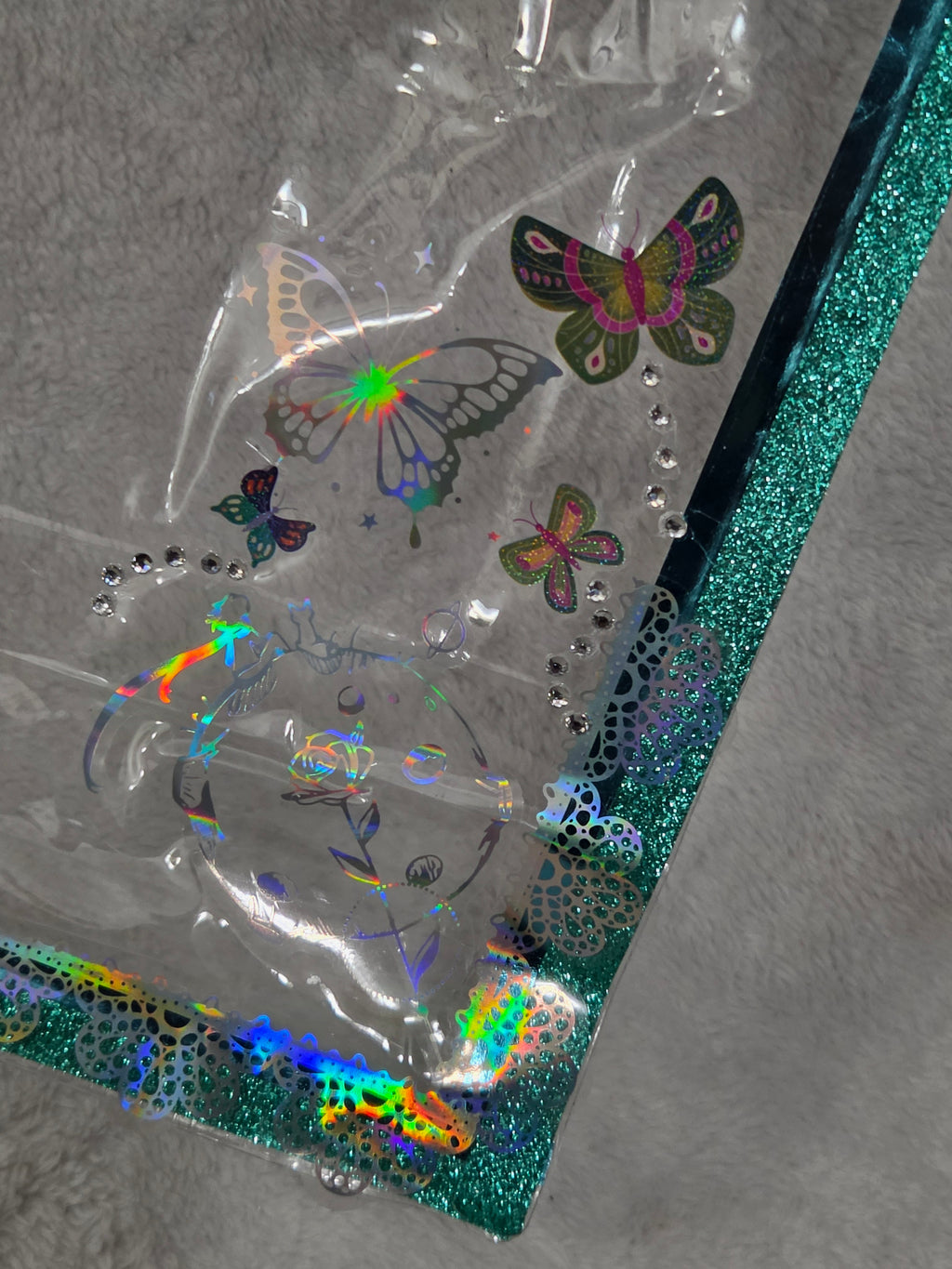 Close-up of holographic iridescent butterfly stickers and rhinestone accents on teal glitter trim bag