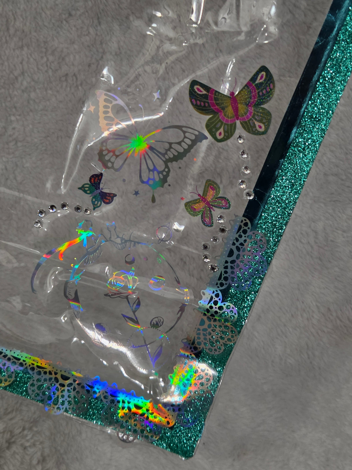Close-up of holographic iridescent butterfly stickers and rhinestone accents on teal glitter trim bag