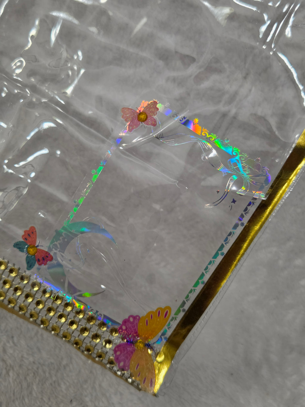 Empty AEFF clear PVC bag with gold metallic trim, gold rhinestone strip bottom, holographic butterfly print and iridescent rectangle frame